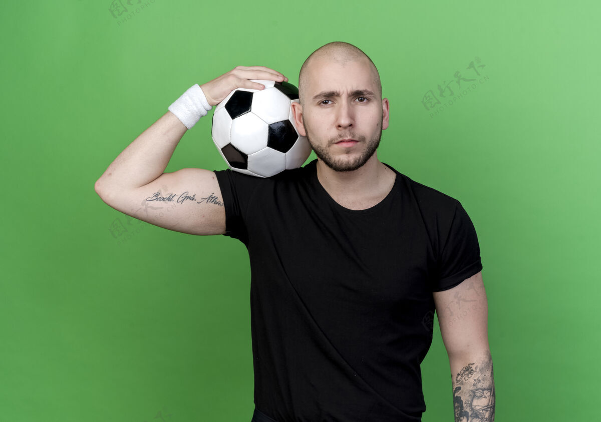 球自信的年轻人戴着腕带 把球放在肩膀上 隔离在绿色的墙上墙穿手势