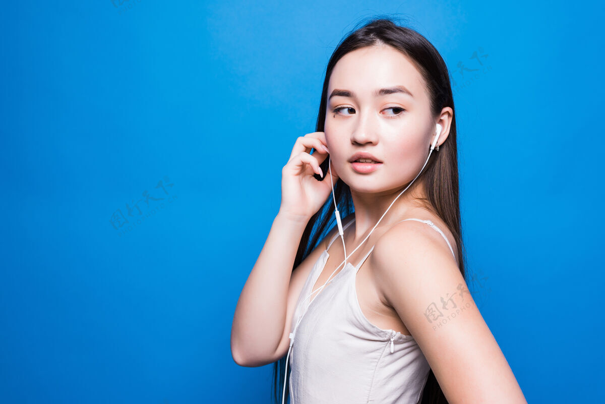 音乐年轻迷人的亚洲女人在蓝色的墙上听音乐女人表情美丽