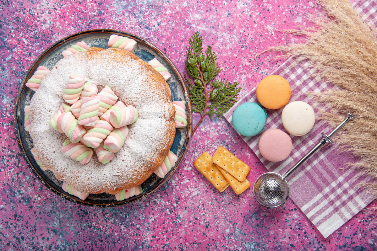 顶视图顶视图的糖粉蛋糕与法国马卡龙和饼干在粉红色的表面饼干麦卡龙饼干