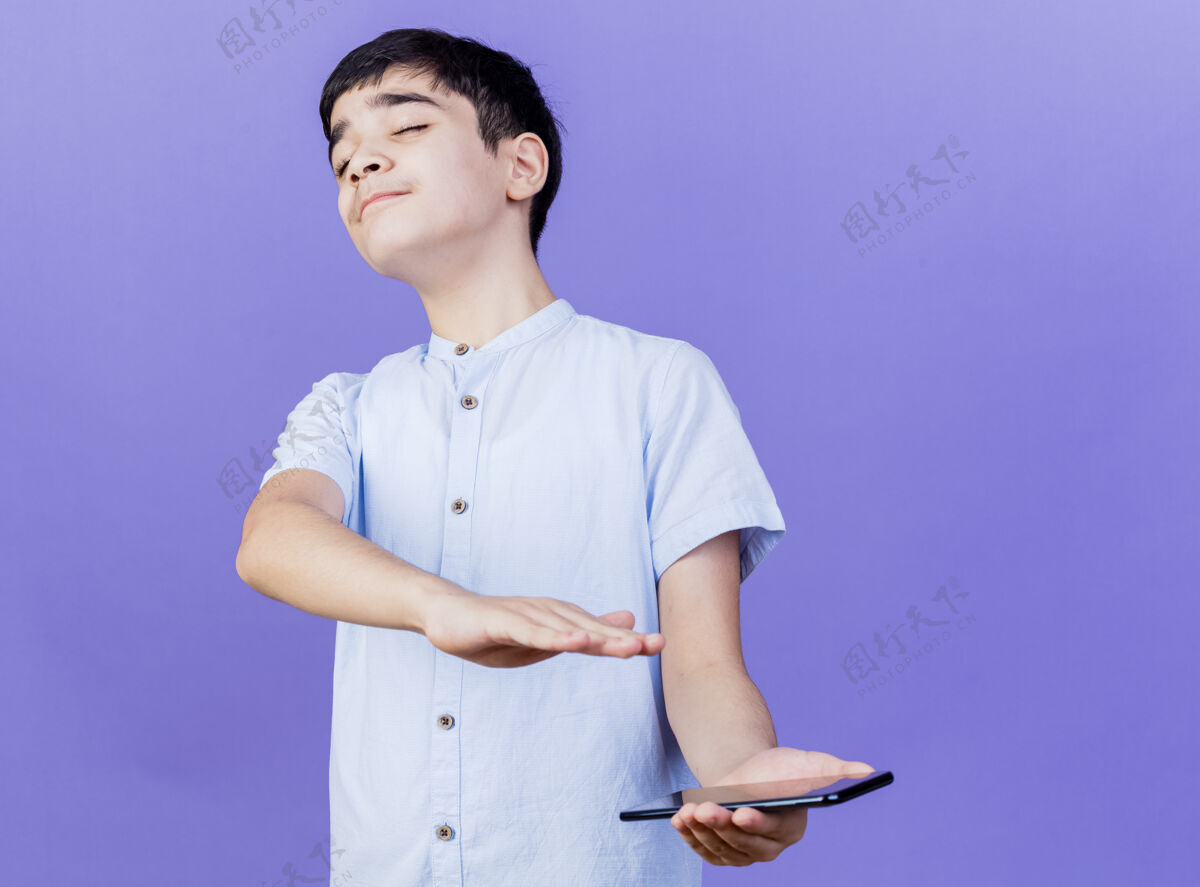 不愉快一个拿着手机的小男孩闭着眼睛不做手势 孤立地站在紫色的墙上电话站着姿势