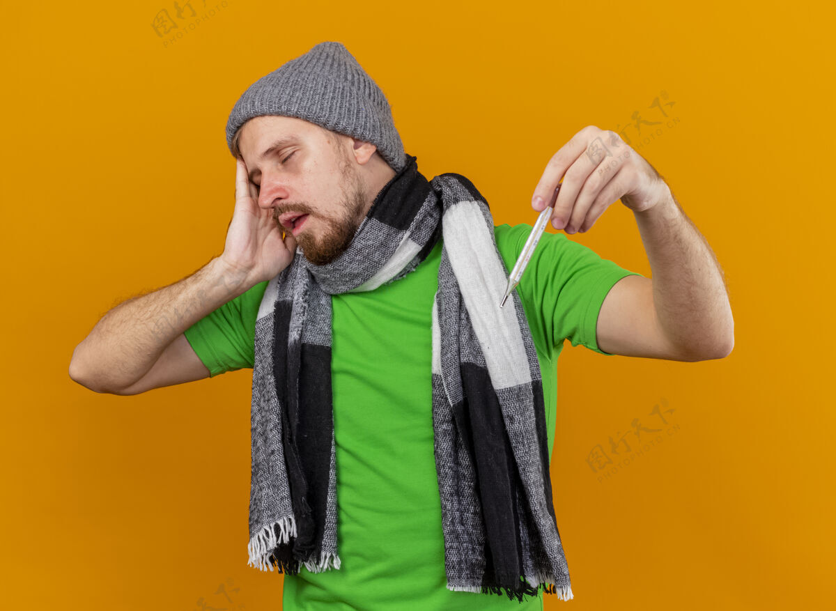 冬天一个戴着冬日帽子 戴着围巾 闭着眼睛 拿着体温计的年轻英俊的病人 在橘色的墙上与世隔绝人感觉表情