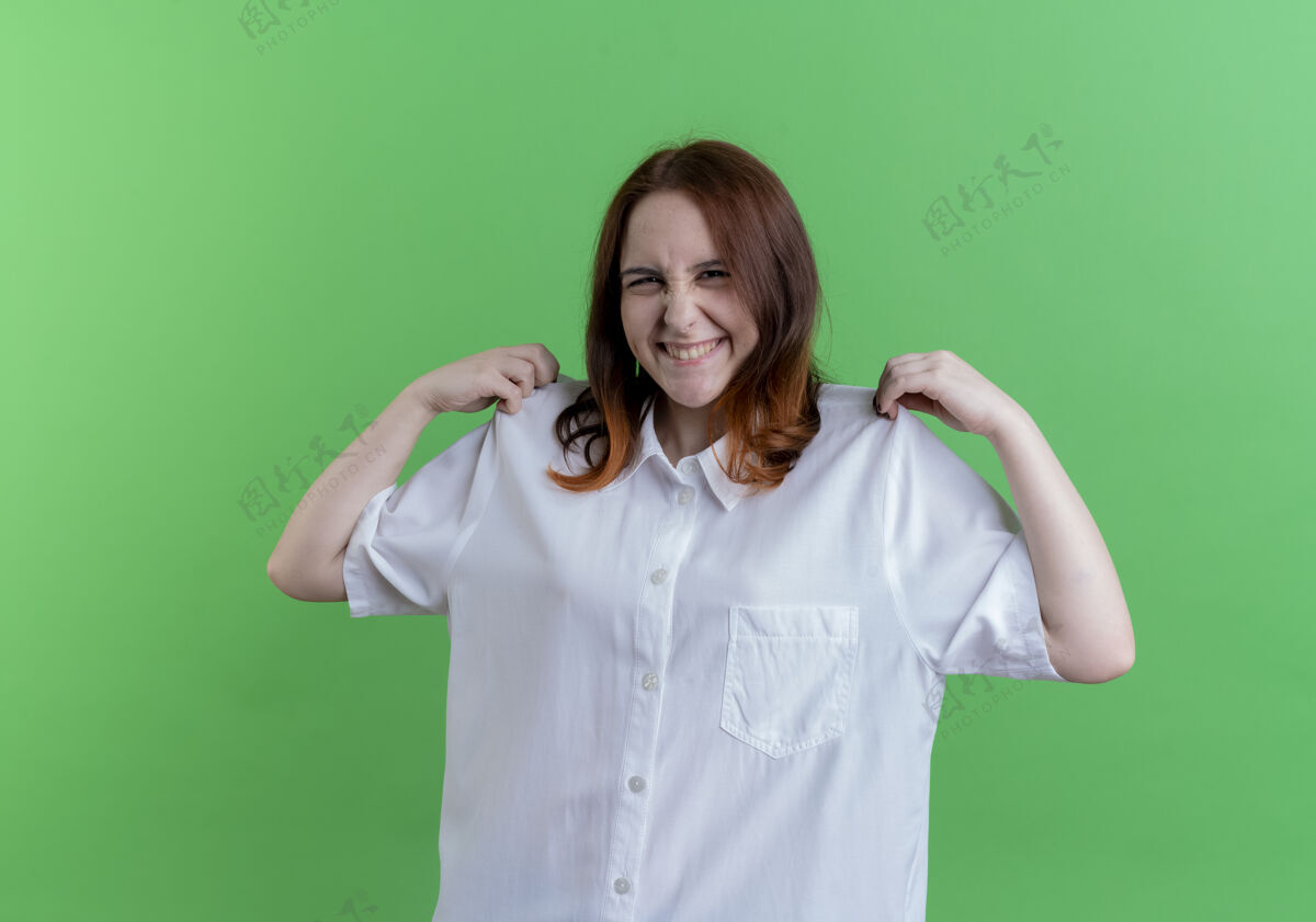 抓取微笑的年轻红发女孩抓起t恤隔离在绿色绿色T恤年轻