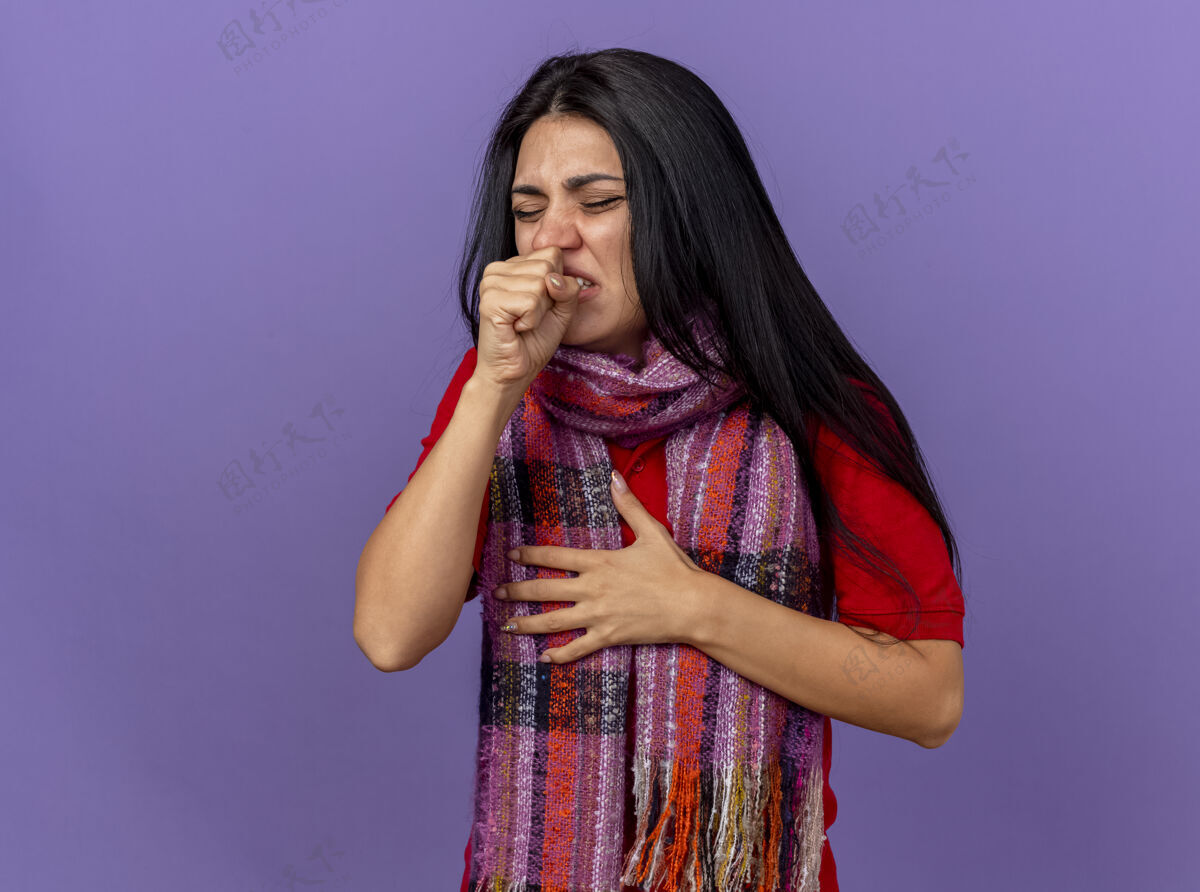 人疼痛的年轻病妇戴着围巾 手放在胸前闭着眼睛咳嗽 拳头紧靠着紫墙上的嘴表情年轻手