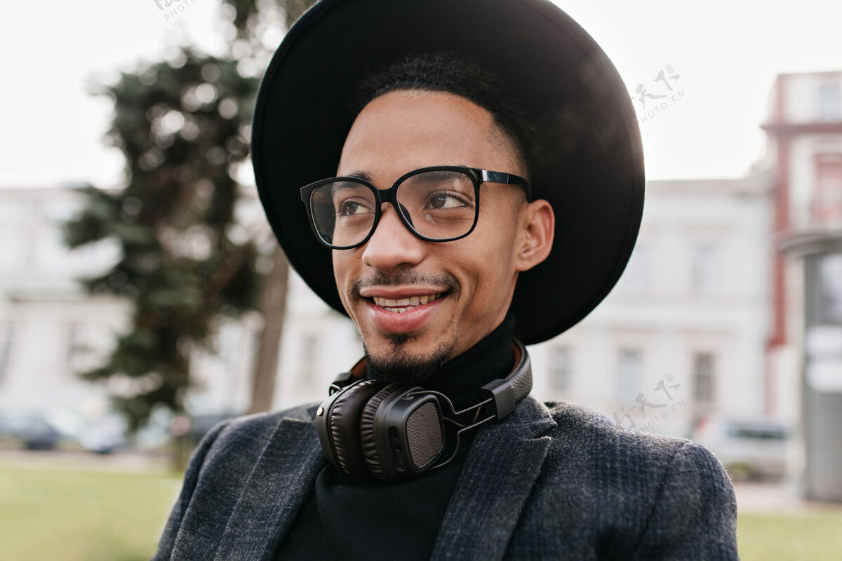 配饰迷人的非洲男人带着真诚的微笑摆姿势戴着眼镜和耳机的可爱黑人男模的户外照片非洲白天肖像