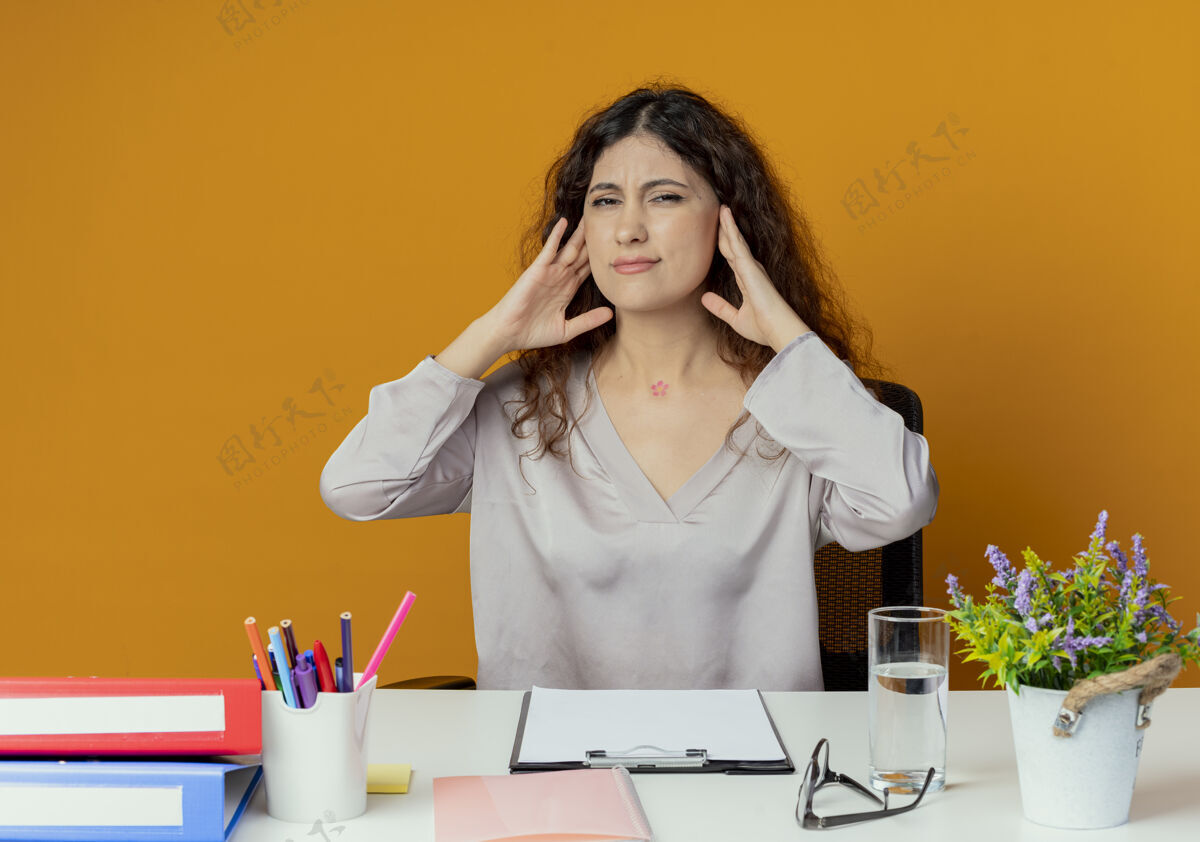 女性疲惫的年轻漂亮的女上班族坐在办公桌前 手放在脖子上 孤立在橘子上橙色年轻办公室