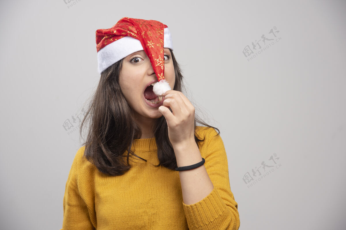 女孩年轻的女人想吃掉圣诞老人的红帽子女士年轻圣诞帽