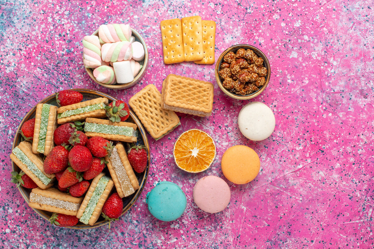 生的美味的华夫饼干俯视图 粉色表面有棉花糖 麦卡龙和新鲜的红色草莓新鲜糖果糖果