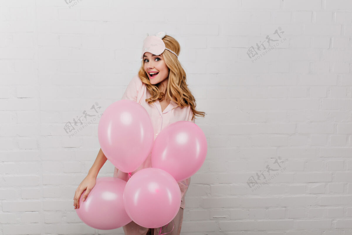 肖像戴着睡衣的快乐女孩站在白色的墙上 手里拿着派对气球一幅美丽的年轻女士在周末早晨庆祝的画像气球放松漂亮