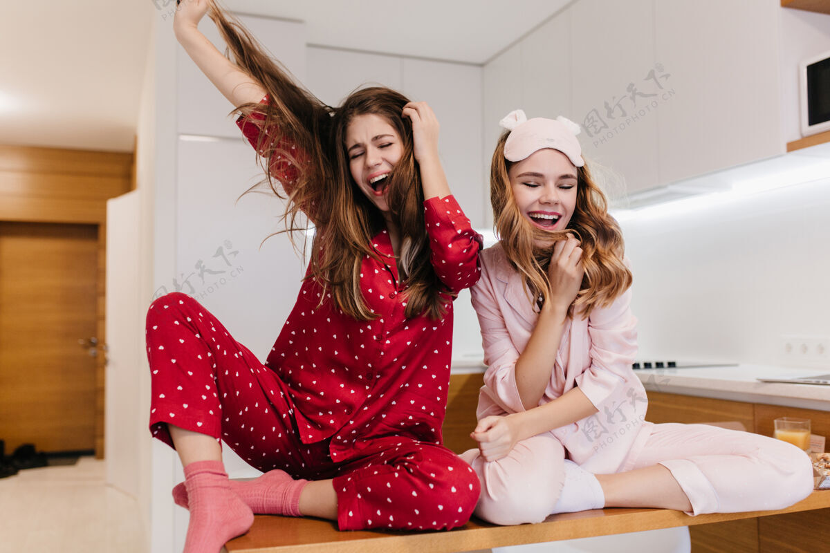 快乐穿着粉色袜子的女孩坐在木桌上 令人毛骨悚然穿着粉色睡衣的可爱年轻女子在厨房里玩得很开心的室内照片快乐金发朋友