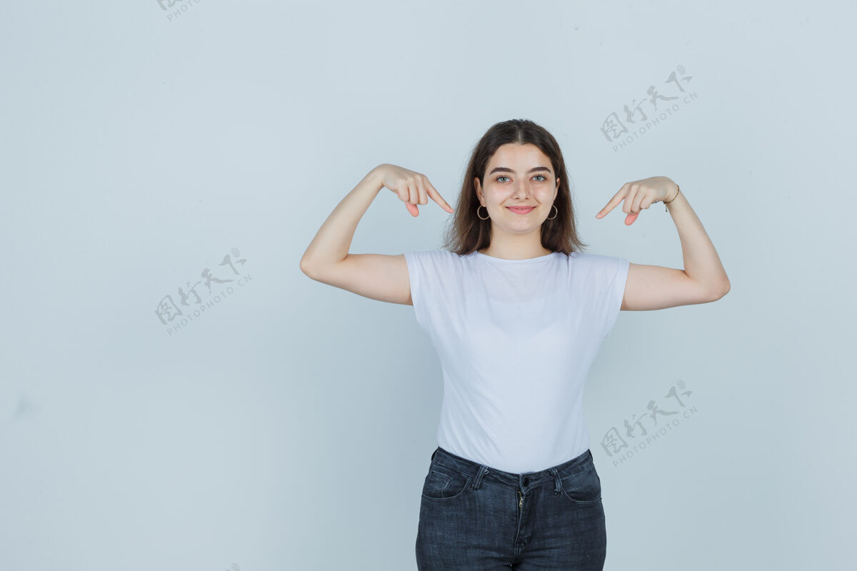 姿势年轻女孩指着自己在t恤 牛仔裤和看起来自信 前视图漂亮亚洲人她自己