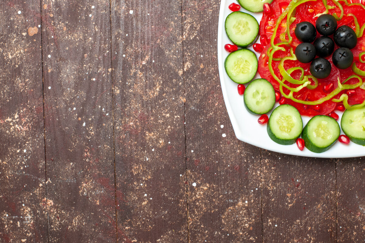 乡村风味俯视图：棕色乡村书桌上盘子里放着切片黄瓜和橄榄 食谱沙拉蔬菜维生素健康蔬菜晚餐风景