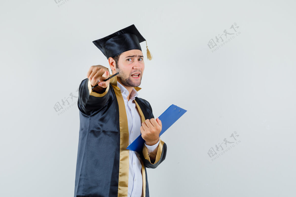 愤怒一个穿着毕业制服的年轻人拿着剪贴板 指着镜头怒气冲冲地看着前方肖像成人胡须