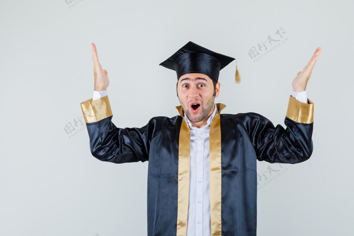 休闲年轻的男学生穿着毕业制服举手 看上去很高兴 正面照孩子制服年轻