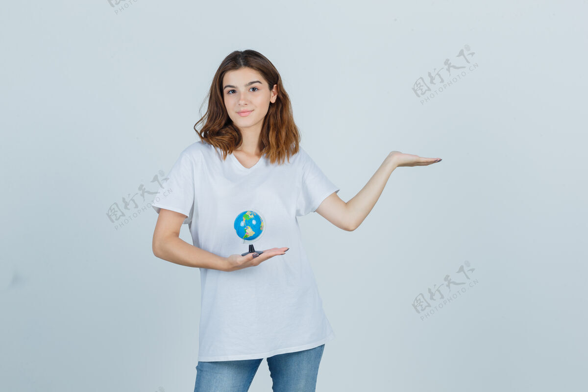 而穿着t恤 牛仔裤的年轻女士拿着地球仪 一边展示着一些东西 一边看起来很自信 正对着前方看人控股女性