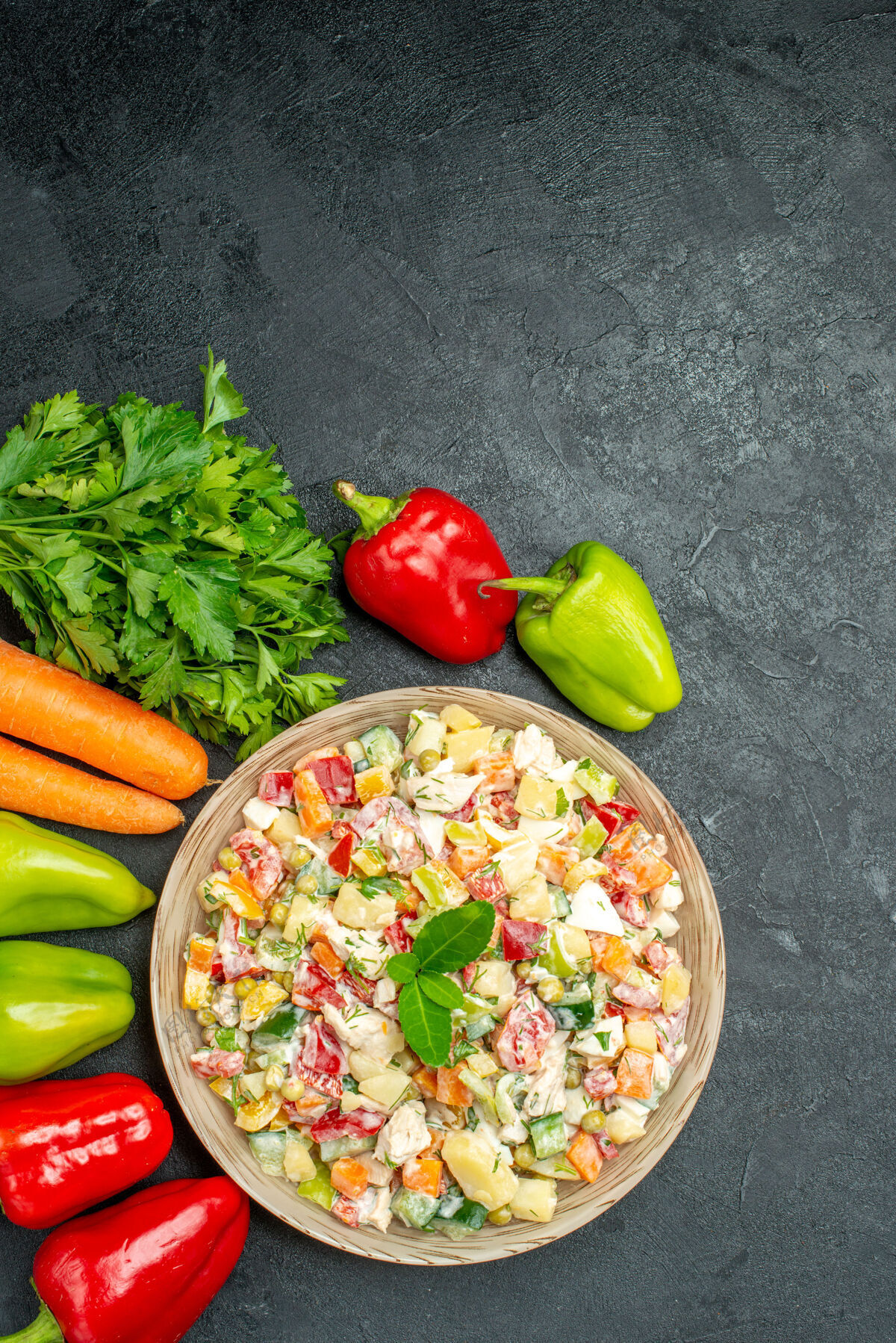 蔬菜深灰色桌子上一碗蔬菜沙拉的顶视图 旁边有胡萝卜 蔬菜和甜椒甜椒甜椒午餐