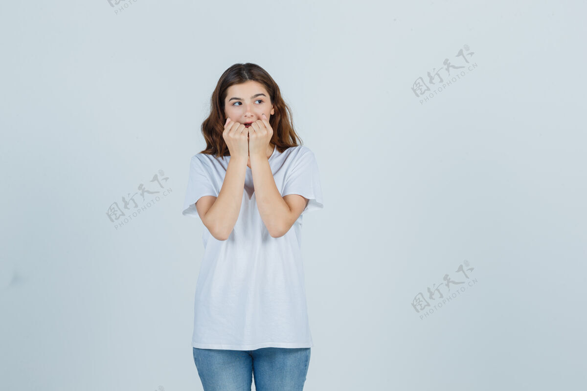 模特穿着白色t恤的年轻女孩情绪激动地咬着拳头 看上去很焦虑正面图时尚面具人