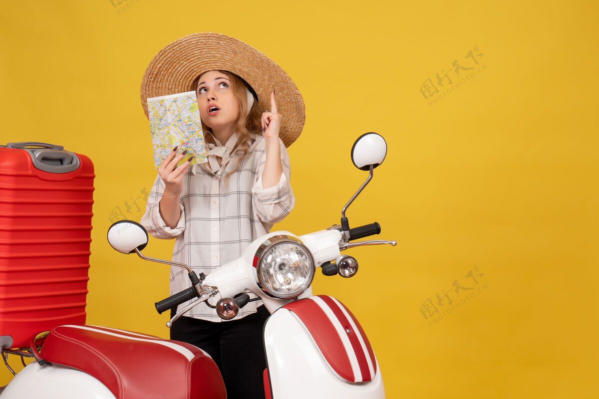 年轻女子俯视图：自信的年轻女子戴着帽子 坐在摩托车上 拿着地图向上指摩托车帽子车辆