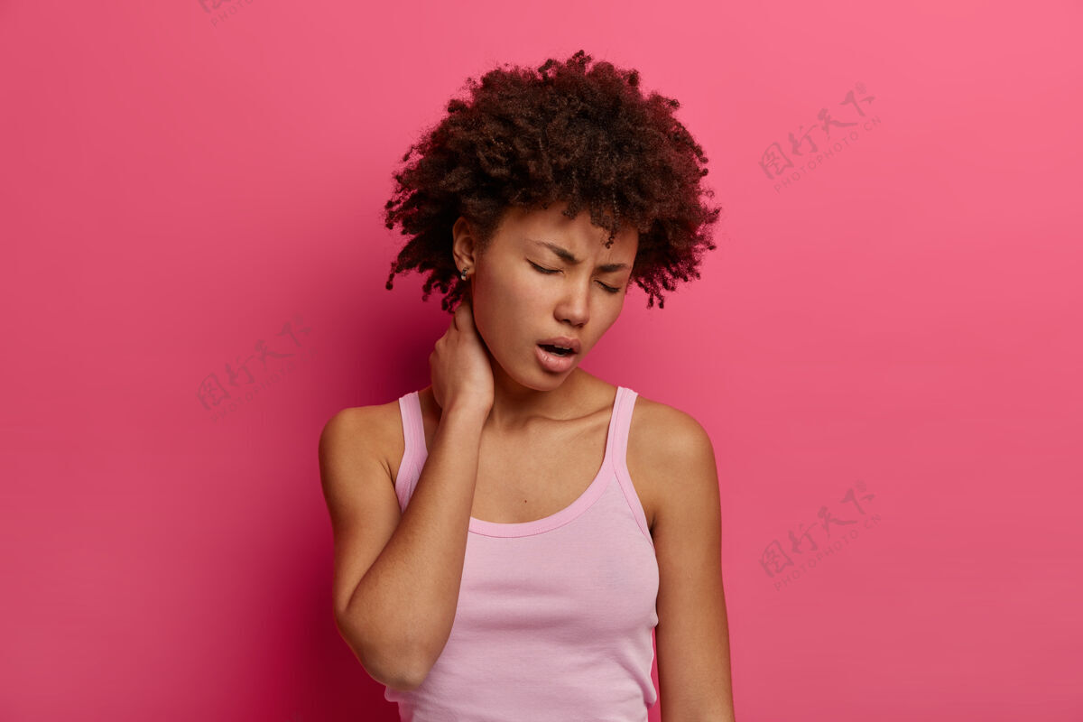 女孩痛苦的女人抚摸脖子 患有背部或脊椎疾病 打呵欠和闭上眼睛 有疲惫的表情 穿着随意 有痛苦的感觉 孤立在粉红色的墙壁卷曲民族疾病