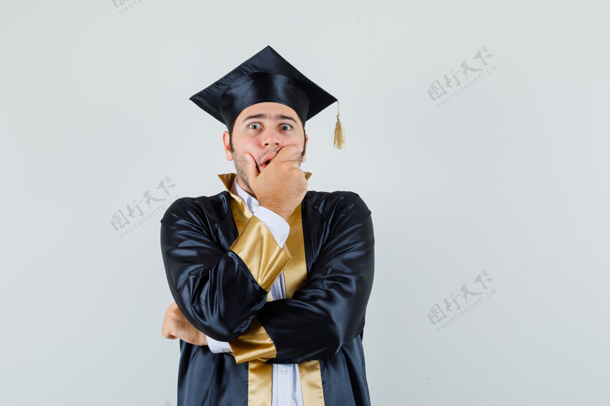 年轻穿着毕业制服的年轻人手捂着嘴 看上去很惊慌正视图肖像自信成功