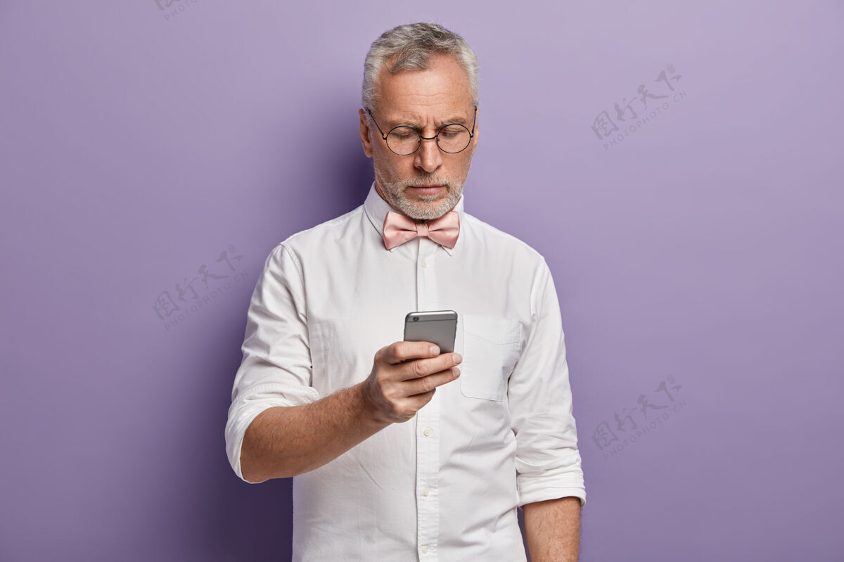 肖像穿着白衬衫和粉色领结的老人拿着电话老人人