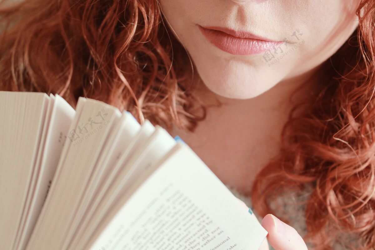 休闲一个红头发的年轻女性在灯光下拿着一本书的特写镜头年轻青春放松