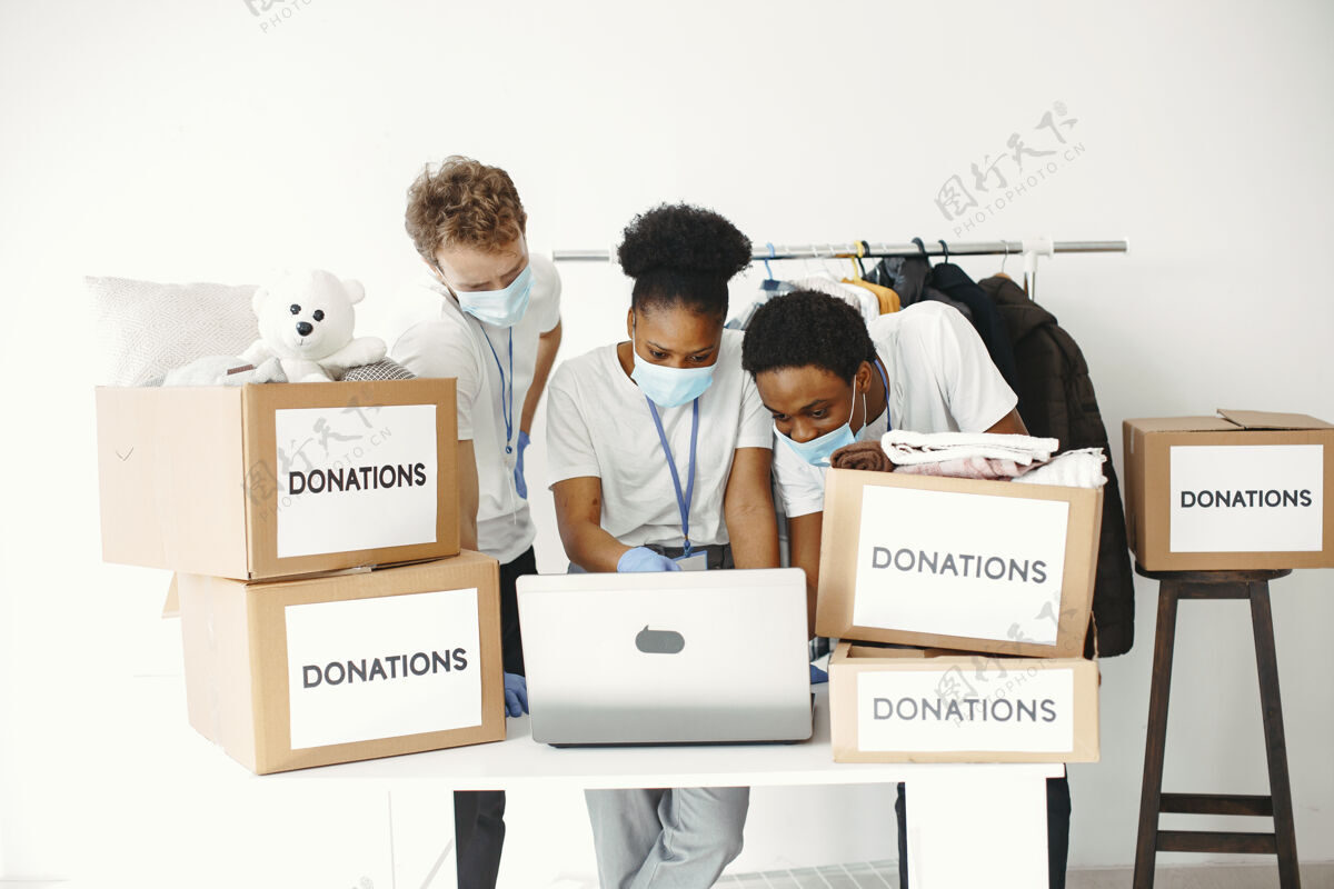 志愿者带着复选框的男男女女戴着面具的志愿者带着笔记本电脑盒子带着人道主义援助流行病工作组织