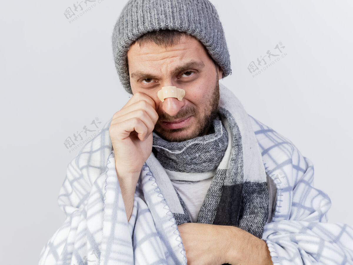 年轻的哭泣的年轻病夫戴着冬天的帽子 围巾裹着格子布 鼻子上贴着灰泥 隔离在白色的背景上包装哭疾病