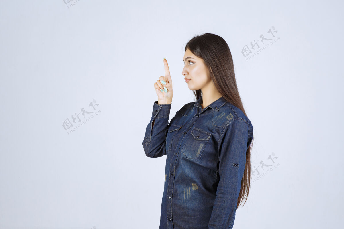工人穿着牛仔衫的年轻女子举起双手 指着上面的东西成人年轻人人