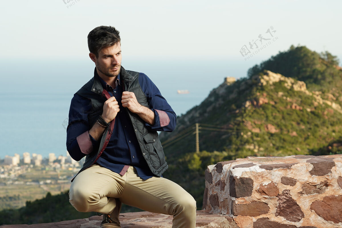 肖像穿着蓝色衬衫和黑色夹克的年轻西班牙裔男模在石墙旁摆姿势块绅士砖头