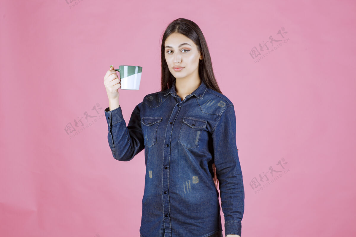 热年轻女子拿着一个白绿色的咖啡杯 闻着女性姿势年轻