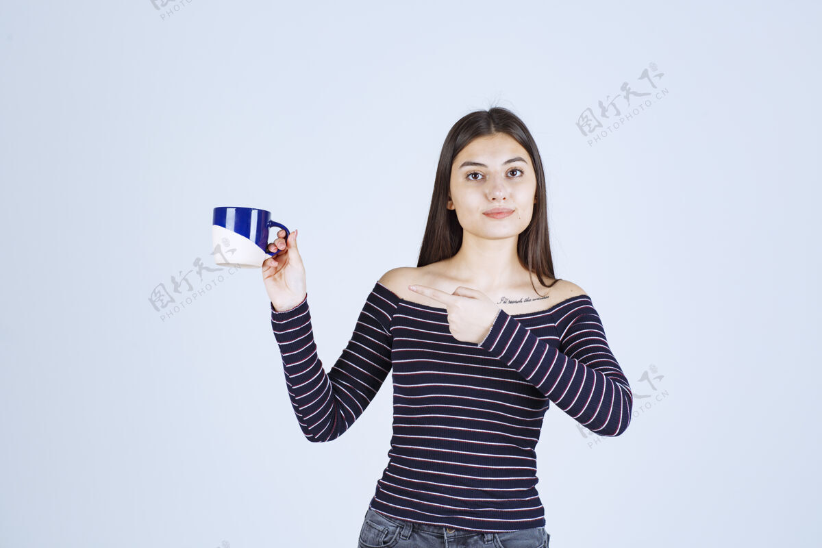 聪明穿着条纹衬衫的女孩拿着一个咖啡杯 展示着享受的标志人体模特成年人人类