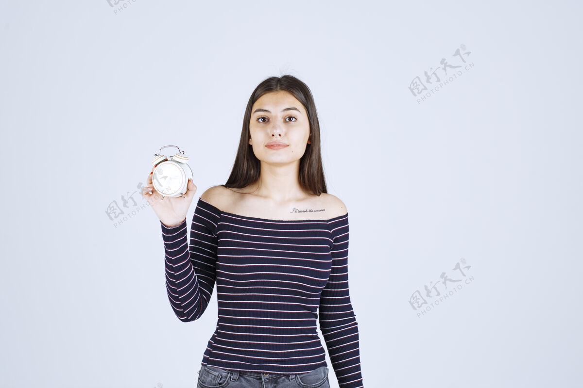 女人穿着条纹衬衫的女孩手里拿着闹钟 把它当作一种新产品来推销职员女售货员销售