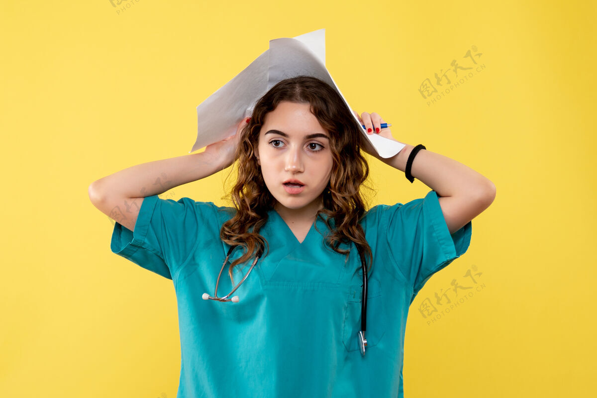 女性正面图女医生穿着医用衬衫拿着纸黄色办公桌大流行病毒制服covid-19情绪分析漂亮成人纸