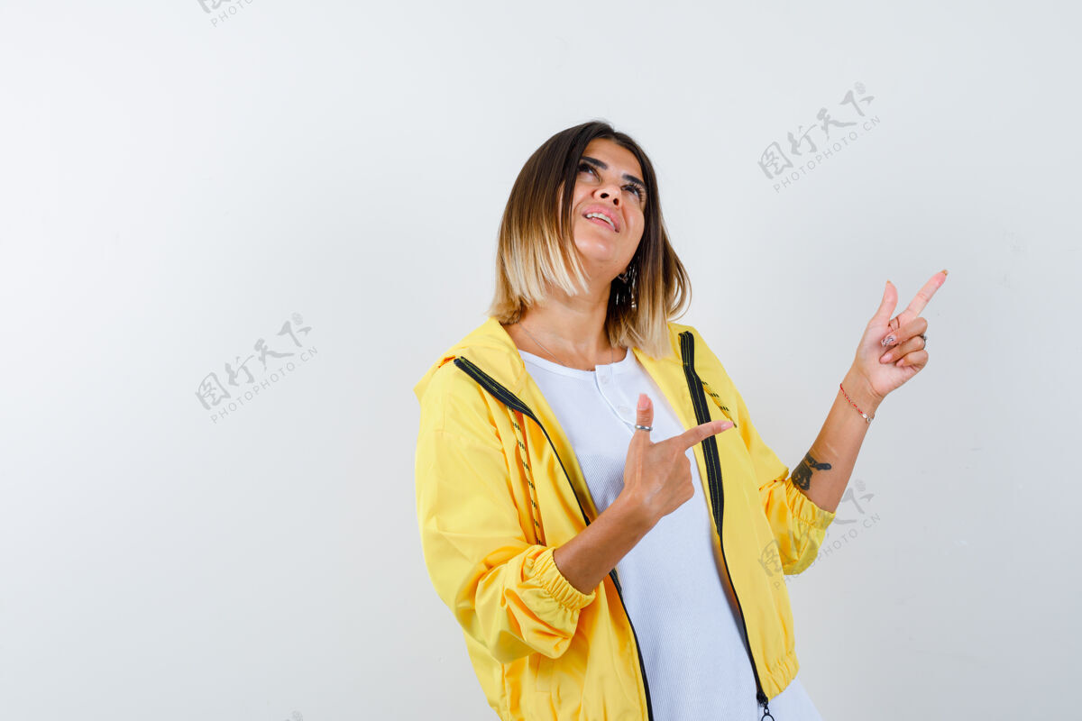 卷发穿着白色t恤 黄色夹克的年轻女孩用食指向上和向右指 看上去很欢快 正面视图乐趣夹克女性