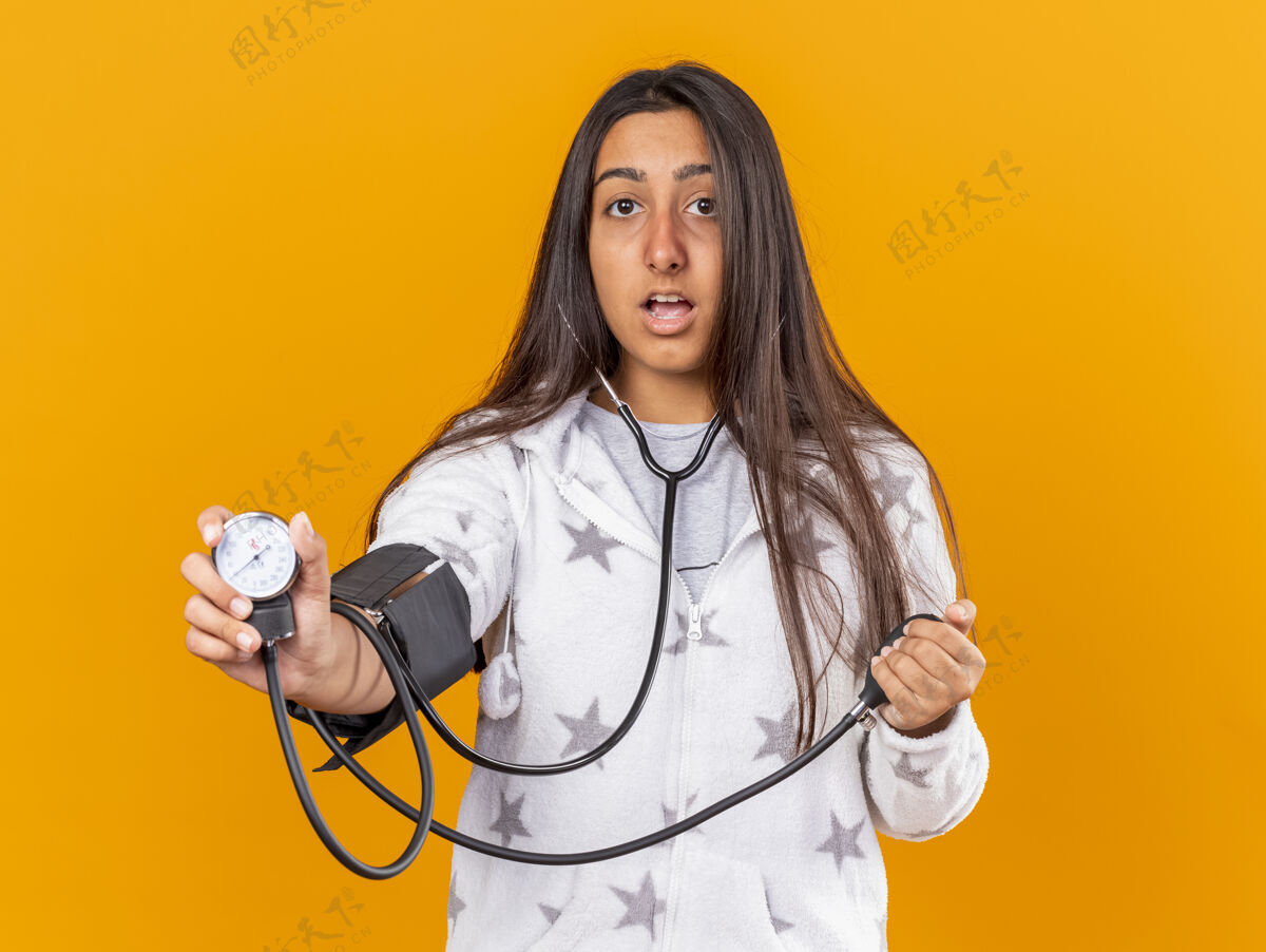 自己惊讶的年轻女孩用隔离在黄色背景上的血压计测量自己的血压惊喜压力女孩