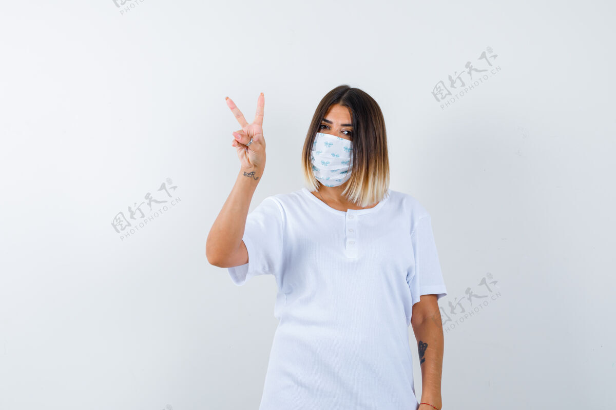 护理身穿t恤的年轻女性 戴着显示胜利标志的面具 看上去很幸运 正面视图眼睛皮肤面具