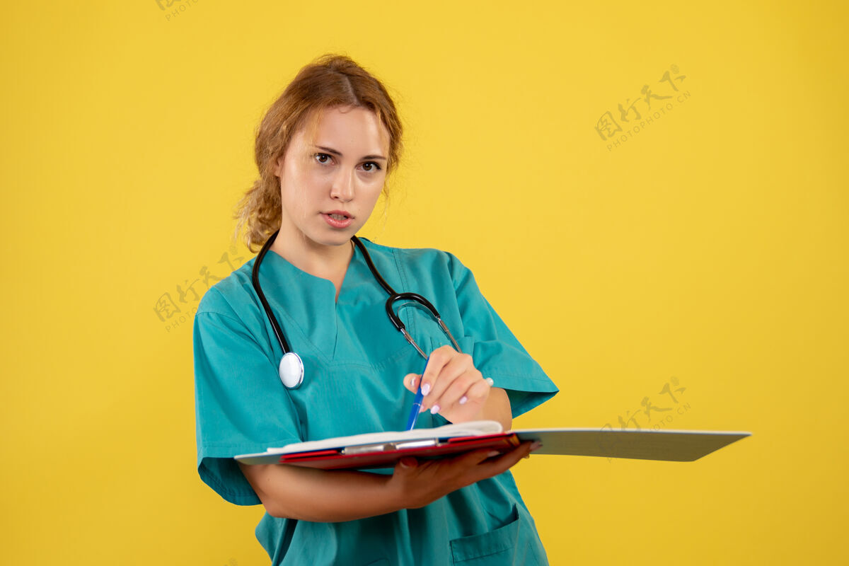 医生黄色墙壁上穿着医疗服的女医生带着论文和分析的正视图听诊器分析女医生