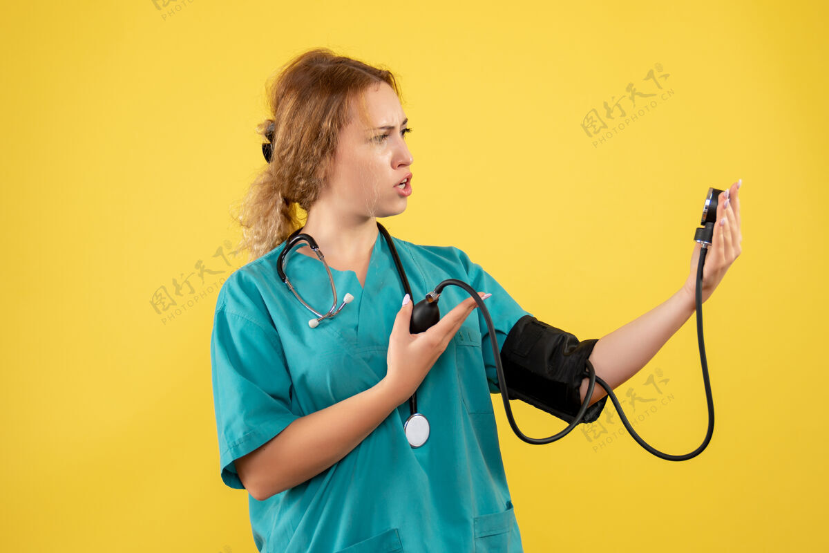 医疗器械身穿医疗服的女医生在黄色墙壁上检查压力的正视图医院西装护士