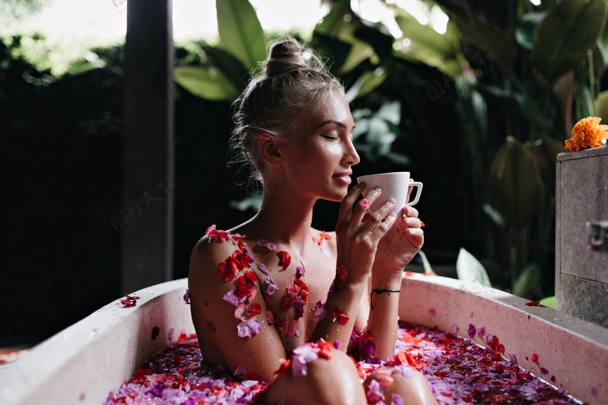 皮肤护理坐在浴缸里闭着眼睛喝着热茶的年轻女子美丽的金发女孩做水疗和享受咖啡的画像玫瑰年轻水疗