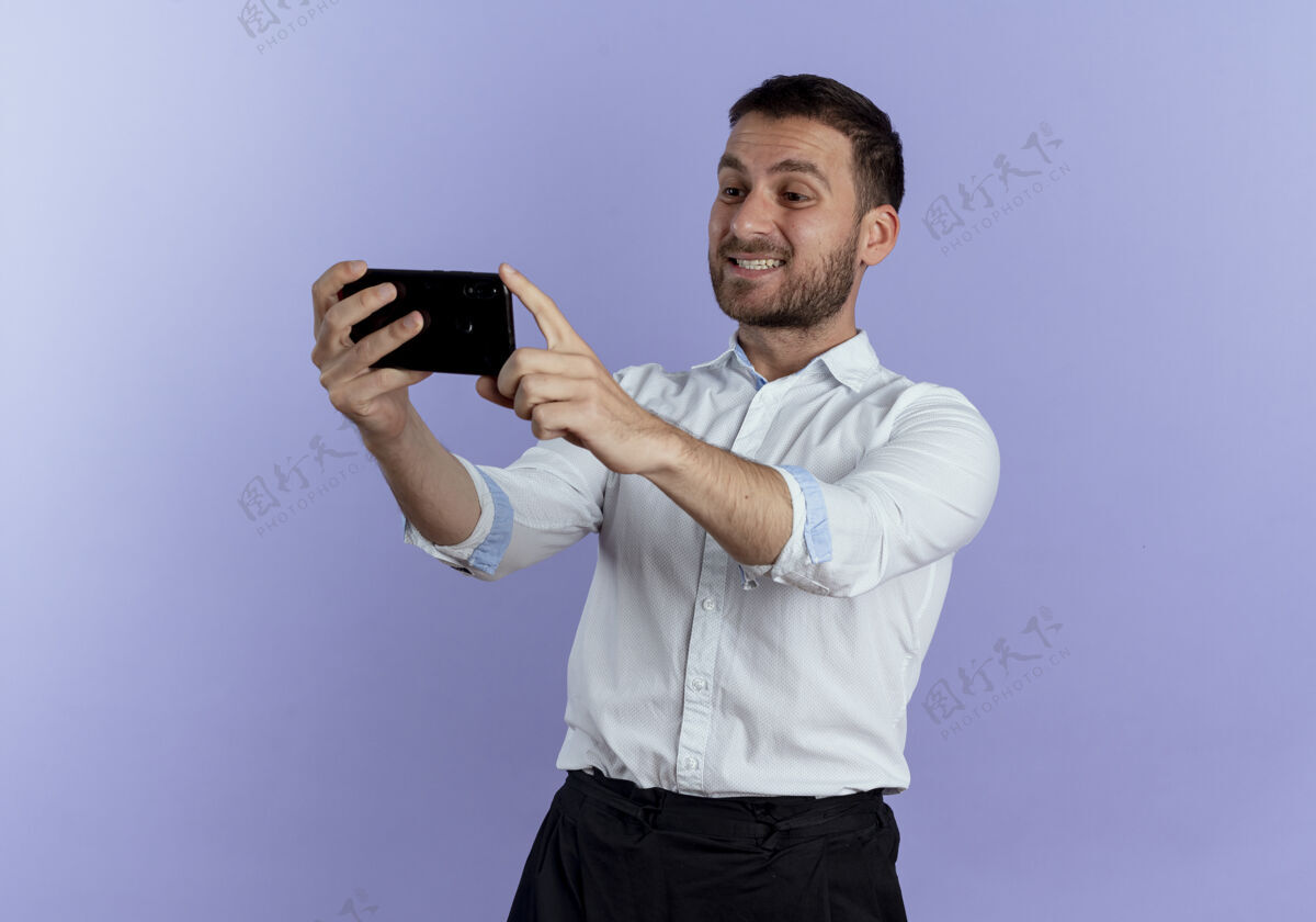 男人笑容可掬的帅哥抱着手机 看着隔离在紫色墙上的手机持有电话优雅