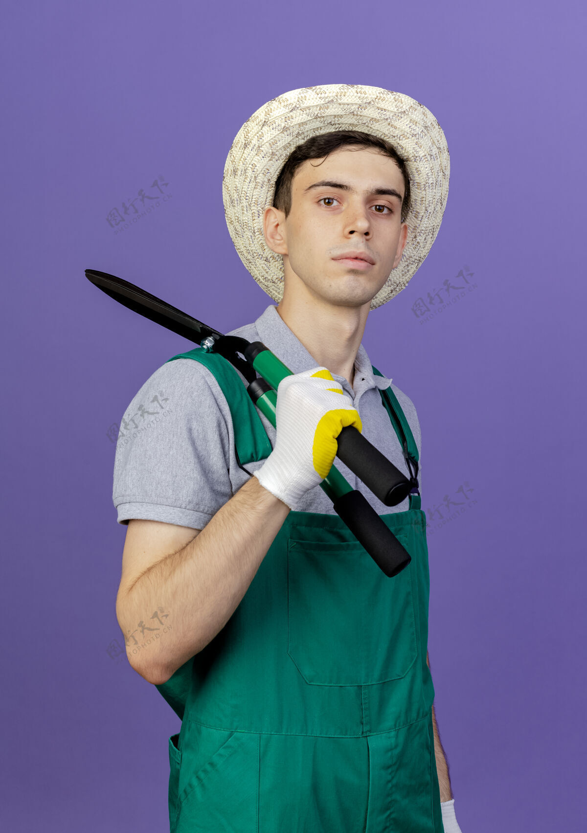 男自信的年轻男园丁戴着园艺帽和手套 肩上拿着剪刀肩膀紫色持有