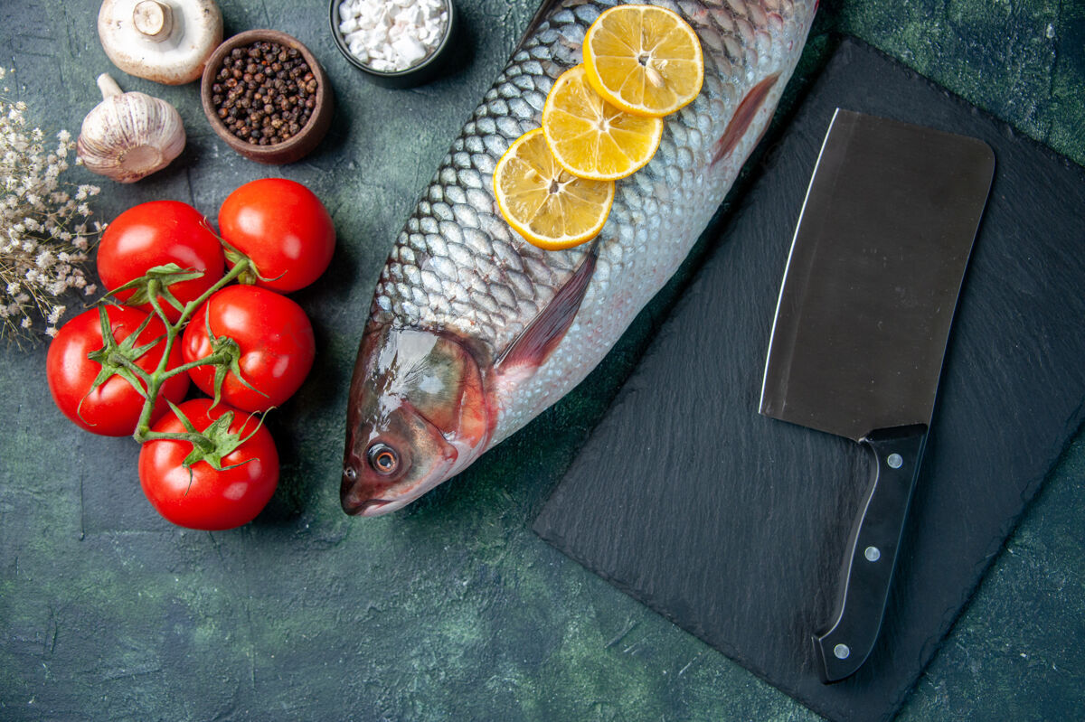 深色在深蓝色的背景上俯瞰新鲜的生鱼片和西红柿肉柠檬食物