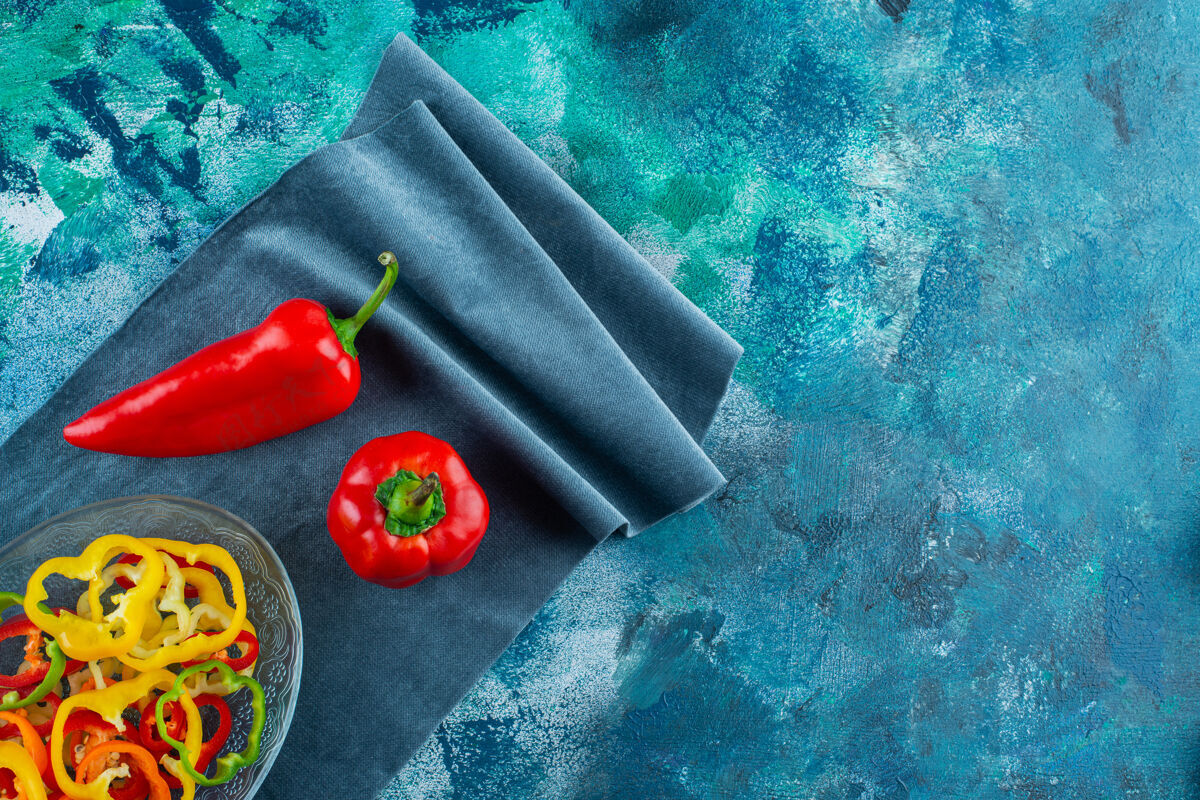 碗把什锦辣椒片放在一个碗里 旁边是一块布上的红辣椒 背景是蓝色的辣椒新鲜胡椒