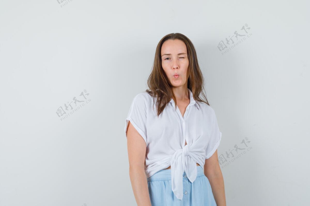 肖像年轻女子眨眼 摆姿势在前面的白色衬衫和浅蓝色裙子 看起来很迷人脸光人