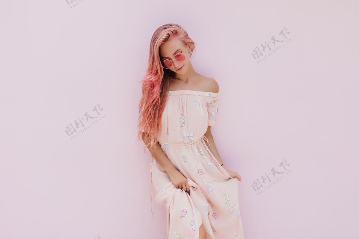 情感一位愁眉苦脸的粉红色头发的年轻女士 一边玩着她的夏装 一边往下看配饰享受微笑