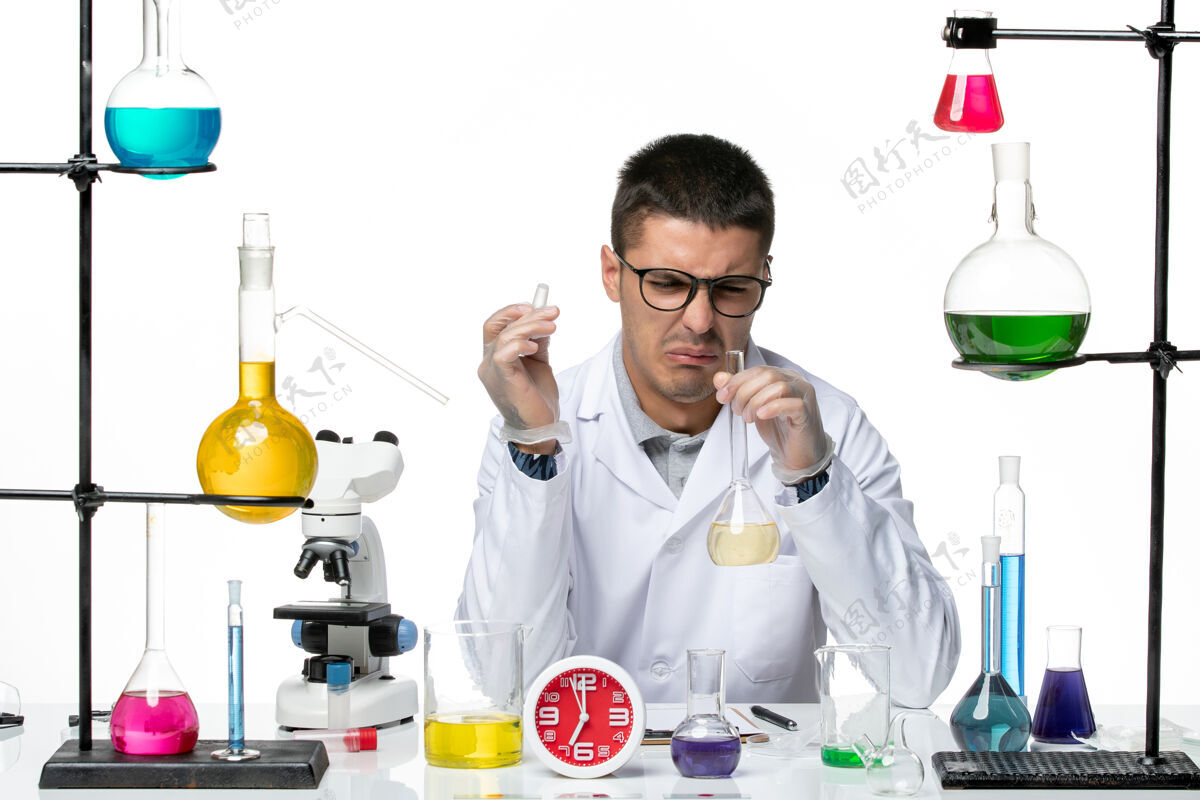药剂师正面图身着白色医疗服的男性化学家在白色办公桌病毒科学实验室用不同的解决方案处理病毒大流行工作服解决方案医学