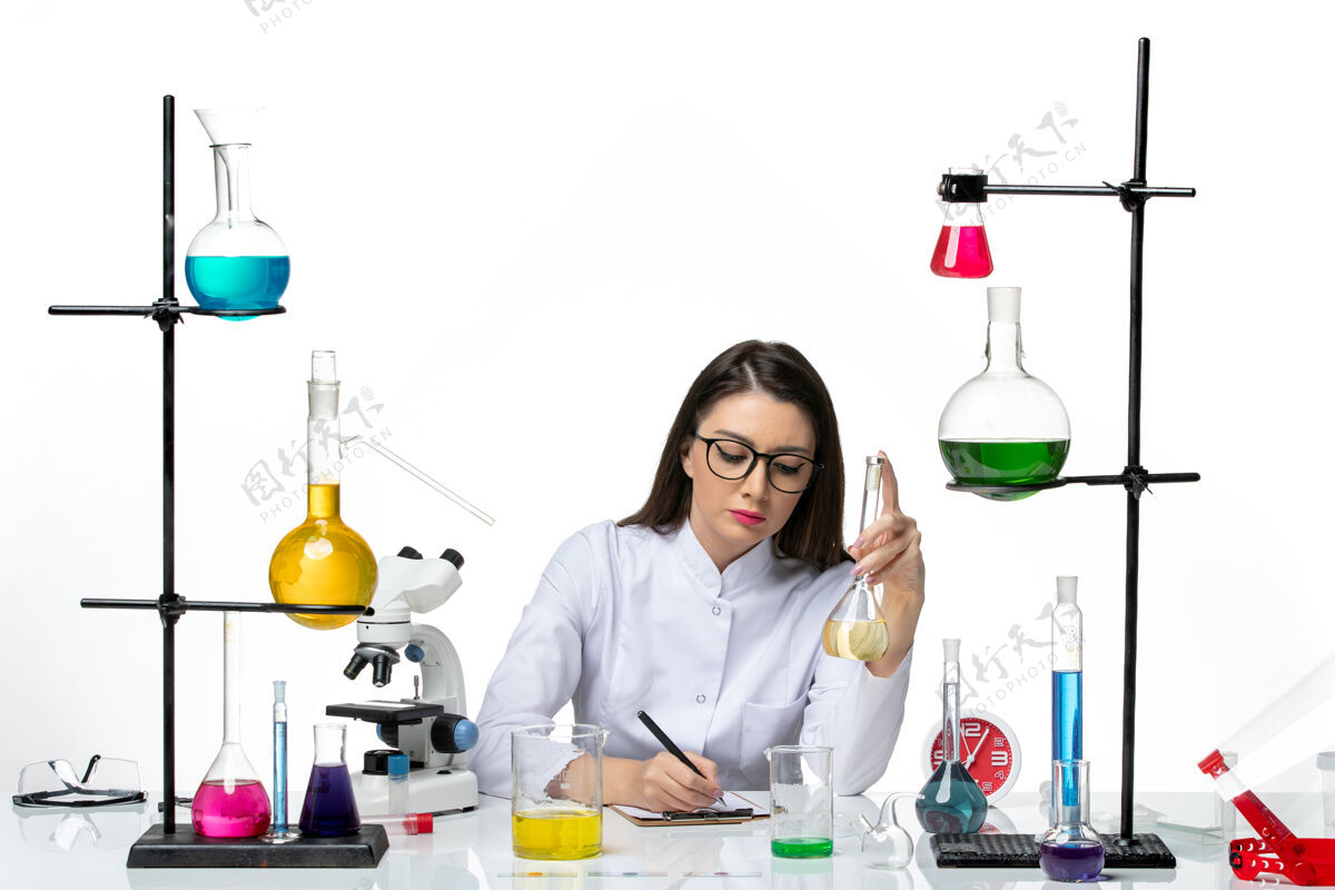 药品前视图穿着白色医疗服的女化学家正在用溶液写关于白色背景的covid科学大流行实验室病毒的笔记玻璃实验室病毒