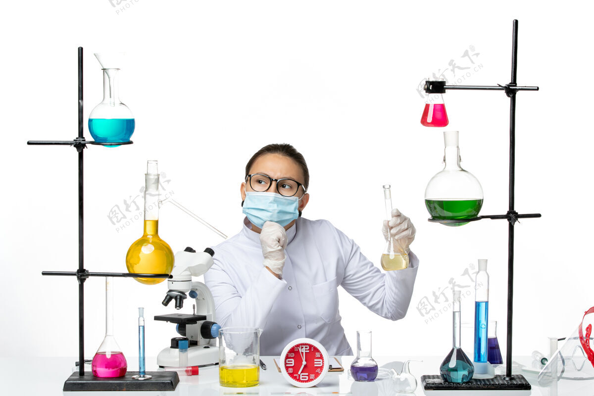 病毒前视图穿着白色医疗服的女化学家带着口罩拿着药水思考白色背景化学家实验室病毒冠状病毒飞溅实验室溶液化学家