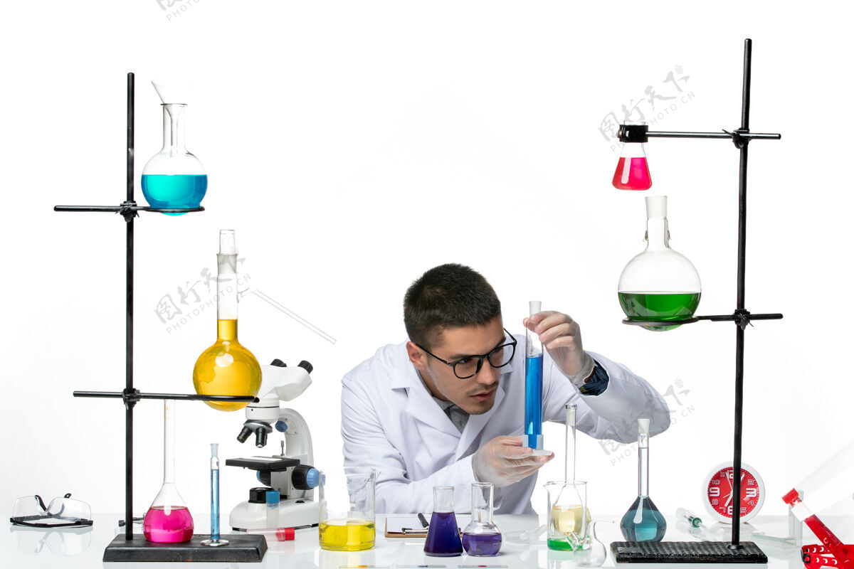 视图正面图身着医疗服的男性化学家坐在浅白背景上拿着溶液病毒冠状病毒-飞溅疾病科学病毒喷溅溶液