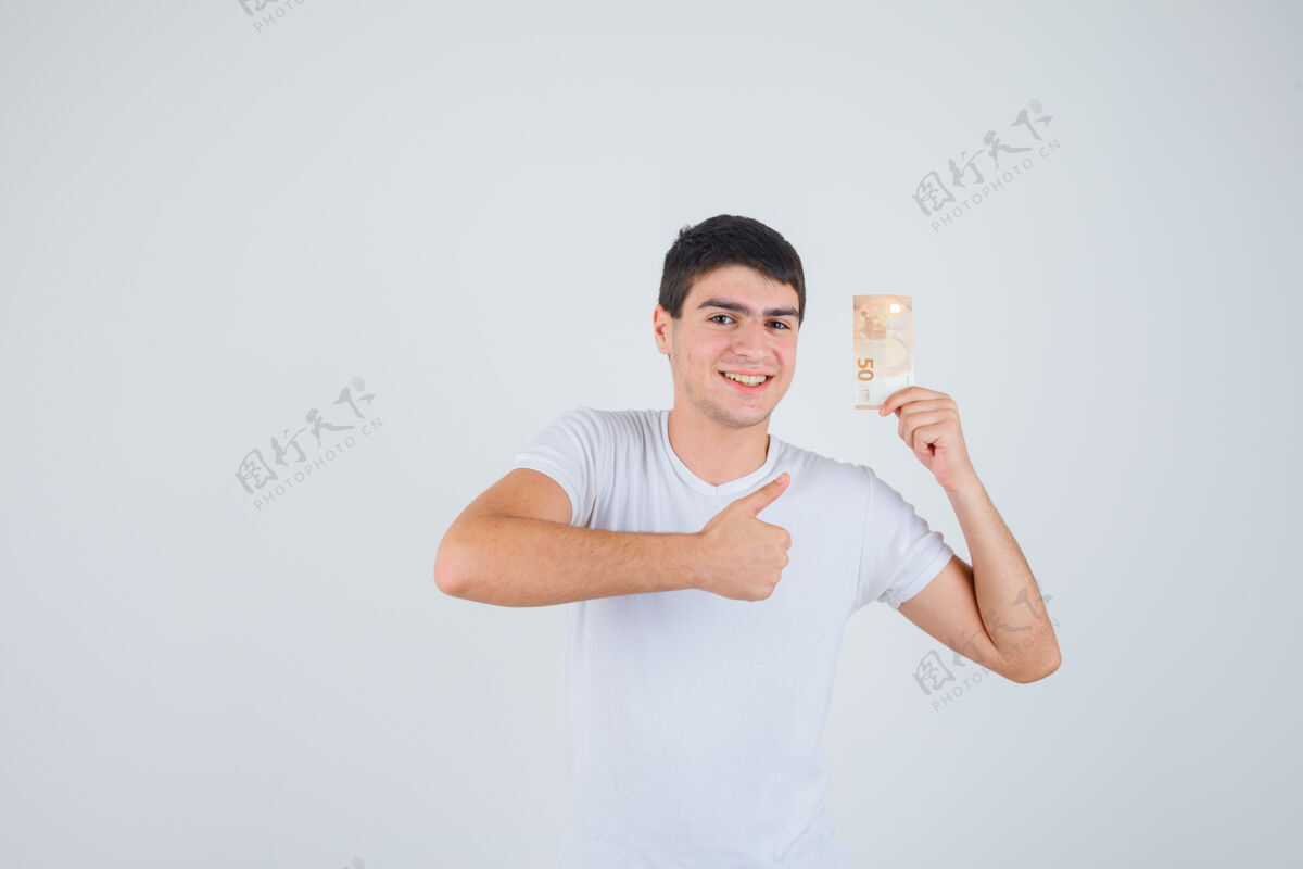拇指身穿t恤的年轻男子手持欧洲钞票 竖起大拇指 看上去很高兴 俯视前方表情微笑人